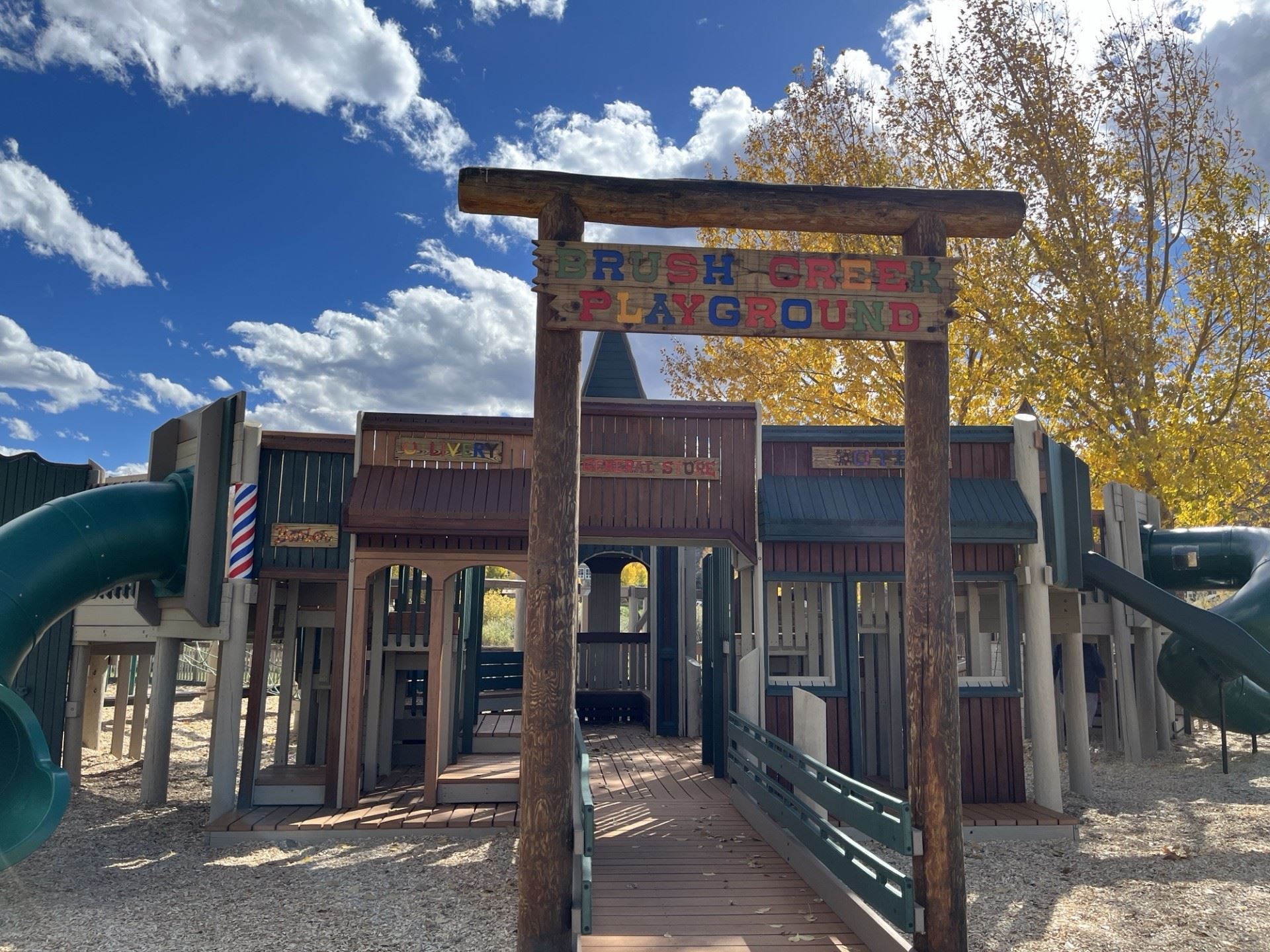 A wooden playground structure with a sign reading "Brush Creek Playground" at the entrance. Th
