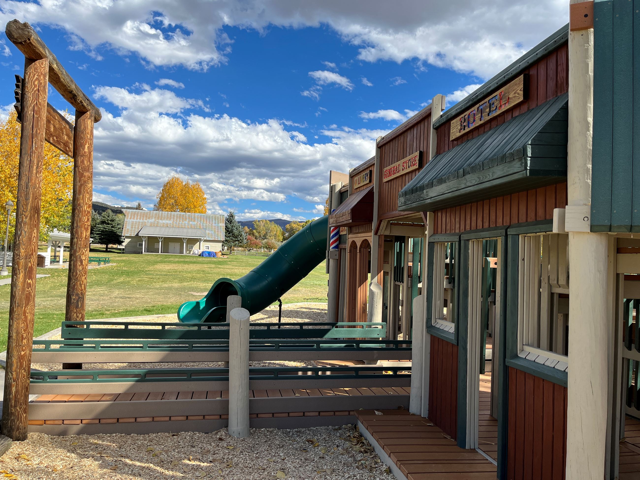 A playground designed to resemble an old western town, featuring wooden structures with facades labe
